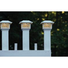 three lamps on top of a white fence with trees in the background