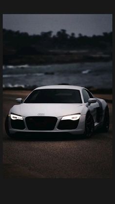 a white sports car is parked on the side of the road by the ocean at night