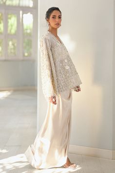 a woman standing in front of a wall wearing a white top and long skirt with an open back