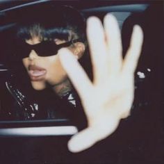 a woman with her hand up in the back seat of a car while wearing sunglasses