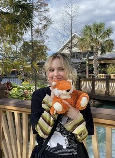 a woman holding a stuffed animal in front of a wooden fence and water area with palm trees