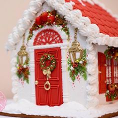 a white gingerbread house with red doors and wreaths on the windows, decorated for christmas