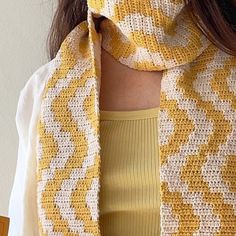 a woman wearing a yellow and white knitted scarf over her shoulder with an orange top underneath