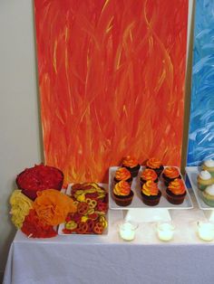 a table topped with cupcakes covered in frosting next to an orange wall