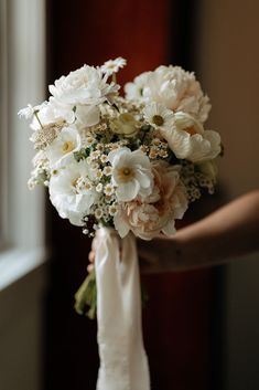 the bride's bouquet is being held by her hand in front of a window