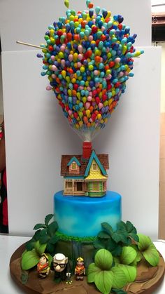 there is a cake that looks like a house on top of the hill with balloons in the air