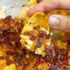 a hand holding a tortilla chip with meat and cheese on it in a pan