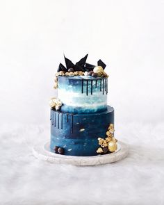 a three tiered cake with blue and white frosting, gold decorations and black birds on top