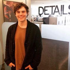 a man standing in an office with his hands in his pockets and smiling at the camera