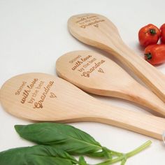 three wooden spoons with engraved names sit next to some tomatoes and basil on a white surface