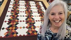 a woman with white hair standing in front of a quilt on the floor and smiling at the camera