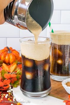 someone pours coffee into two glasses with pumpkins in the background