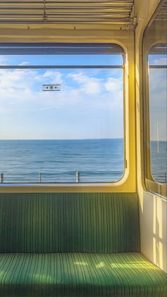 a green bench sitting in front of a window on top of a train next to the ocean