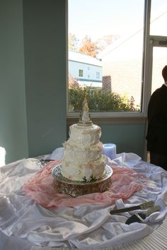 a white wedding cake sitting on top of a table next to a window with people looking out the window