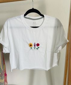 Thank you for your interest! This item is a hand embroidered cropped tee. The sleeves are tiled and stitched and the bottom is a raw edge. The design is 3 different flowers a sun flower, a rose and a lavender branch.  -Men's T-shirt  -size men's M  -Fruit of the loom  -hand embroidred  colors: green, brown, yellow, red, purple White Tee Embroidery, Spring Cotton Crop Top With Floral Embroidery, Spring Floral Embroidery Cotton Crop Top, Casual Floral Embroidery Crop Top For Spring, White Embroidered Cotton Crop Top, Casual White Embroidered Crop Top, Trendy Tops With Custom Embroidery For Spring, Trendy Top With Custom Embroidery For Spring, Casual Cotton Crop Top With Floral Embroidery