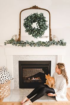 a woman sitting in front of a fire place holding a cat