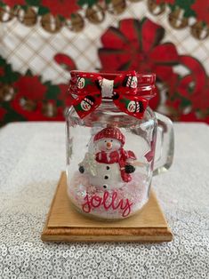 a glass jar with a snowman in it on a wooden board and red bows