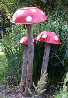 two red mushrooms sitting on top of wooden posts in the grass next to some plants