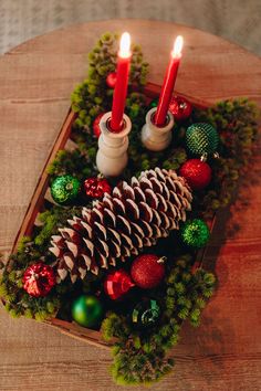 two candles are sitting in a wooden box with pine cones and christmas decorations on it