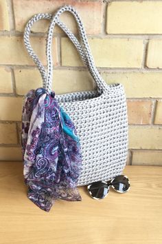 a white purse sitting on top of a wooden table next to sunglasses and a scarf