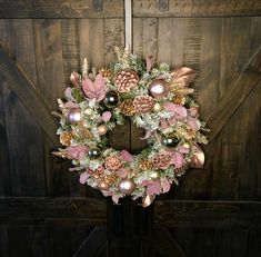 a wreath with pink and gold decorations hanging on a wooden door