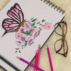 a notebook with a butterfly and flowers on it next to some pencils, reading glasses and a pair of eyeglasses