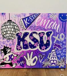 a painting with the word kiss written in purple and white on it, next to a wooden floor