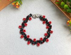 a red and black beaded bracelet sitting on top of a wooden table next to flowers