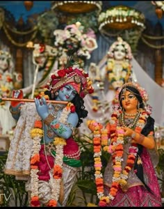 two statues of hindu deities in front of a decorated stage with flowers and garlands