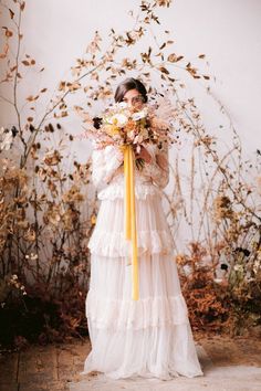 a woman in a white dress holding a yellow ribbon around her neck and wearing a flower crown