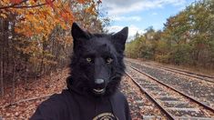 a person wearing a black wolf mask on the train tracks