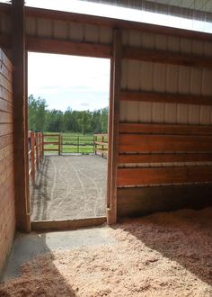 an open door to a stable with horses in the stalls and hay on the ground