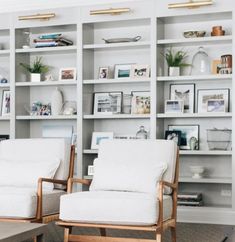 two white chairs sitting in front of a bookshelf filled with pictures and photos