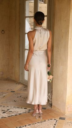 a woman in a white dress is standing near a door and looking at the floor