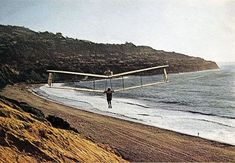 an airplane is flying over the beach with two people walking on it and another person standing in the water