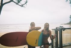 two women standing next to each other holding surfboards