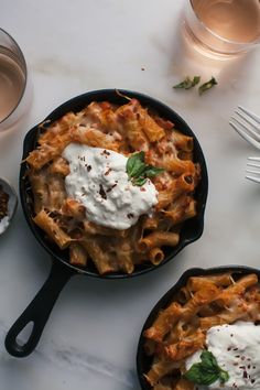 two skillets filled with food on top of a white marble counter next to silverware