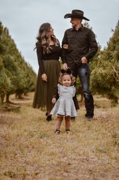 a man, woman and child standing in an apple orchard with one holding the other's hand