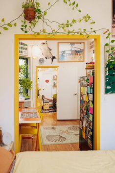 a room with a bed, desk and plants on the wall above it in front of a door