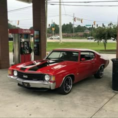 a red muscle car parked in front of a gas station with an old fashioned pump