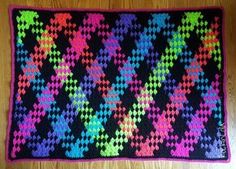 a multicolored crocheted rug on a wooden floor with a black background