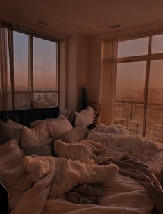 an unmade bed is in front of two large windows with the city view outside