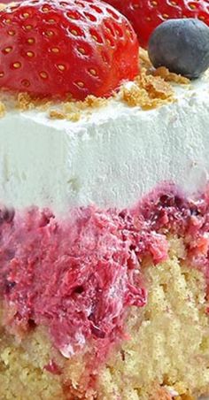 a close up of a cake with strawberries on top and blueberries on the side