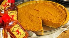 a pumpkin pie sitting on top of a wooden table next to bottles of whiskey and sauce