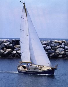 a sailboat with white sails is in the water next to some rocks and boulders