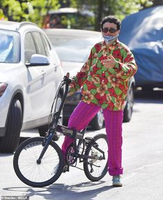 a man in colorful clothing standing next to a bicycle on the street with cars behind him