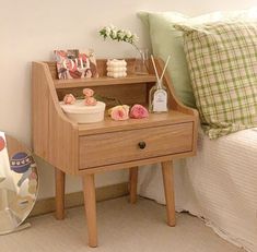 a small wooden table with some flowers on it next to a bed and pillows in a room