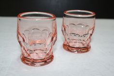 two pink glass cups sitting on top of a white tablecloth covered table next to each other