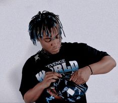 a young man with dreadlocks is looking at his cell phone while wearing a black t - shirt