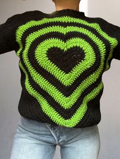 a woman wearing a black and green knitted sweater with a heart on the back